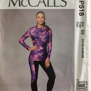 May include: McCall's MP518 sewing pattern featuring a woman wearing a long-sleeved top and leggings. The top has a purple and pink tie-dye pattern with a diagonal zipper. The leggings are black with a purple and pink panel.