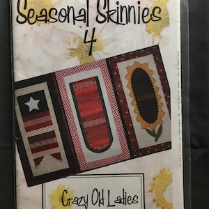 May include: A package for "Seasonal Skinnies 4" by "Crazy Old Ladies" features three fabric panels with patriotic and floral designs. The panels include a star, stripes, and a sunflower. The background has a floral pattern.