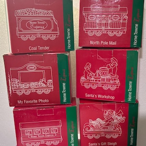 May include: A stack of six red boxes with white line drawings of trains. Each box has a different train car design, including "Coal Tender," "North Pole Mail," "My Favorite Photo," "Santa's Workshop," "Passenger Express," and "Santa's Gift Sleigh."