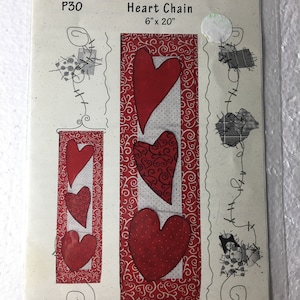 May include: A sewing pattern titled "Heart Chain" by Patch Abilities, Inc. The pattern features red heart designs on a white and red patterned background. The dimensions are 6" x 20".