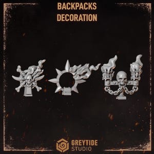 May include: Three grey miniature backpack decorations featuring the text BACKPACKS DECORATION. The items include a skull with crossed bones and flames, a spiked circular frame with flames, and a skull flanked by two torches and hanging chains.