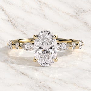 Pode incluir: Um anel de ouro amarelo com um grande diamante central de corte oval preso por quatro garras. A banda é adornada com dois diamantes de corte marquise e dois diamantes de corte redondo em cada lado, criando um design simétrico com pedras.