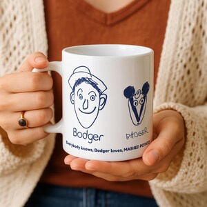 May include: White ceramic mug with navy blue cartoon illustrations of a man and a badger. The man is labelled "Bodger" and the badger is labelled "Badger". The text at the bottom reads "Everybody knows, Badger loves, MASHED POTATO."