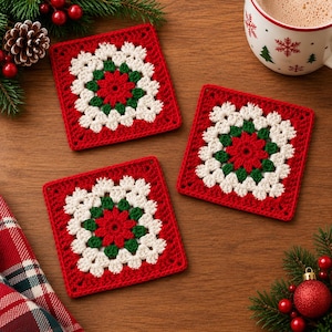 May include: Three square crochet coasters featuring a central red flower motif surrounded by a ring of dark green yarn and an outer border of white yarn, finished with a final red edge. The coasters are arranged on a wooden surface.