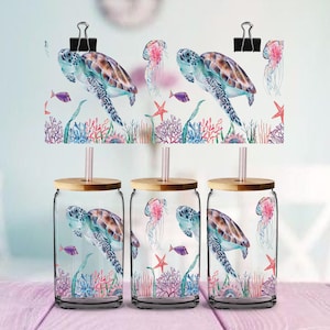 May include: Three glass tumblers with bamboo lids and straws, each with a watercolour design of a sea turtle, jellyfish, fish, and coral. The design is also printed on a paper held by binder clips.