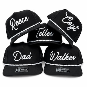 May include: A stack of five black baseball caps with white rope trim across the brim. Each cap features white embroidered script text reading Reece, Coyt, Teller, Dad, and Walker. The hats have perforated side panels and a 10 10 HATS label.