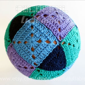 Puede incluir: Una bola de crochet hecha de cuadrados coloridos en tonos de azul, verde y morado. La bola está hecha de cuadrados de la abuela con un diseño texturizado y calado.
