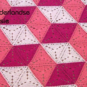 Op de afbeelding: Een gehaakt deken met een 3D geometrisch patroon in roze, wit en koraal. Het deken is gemaakt met een herhalend patroon van vierkanten en driehoeken. De tekst "Nederlandse versie" is zichtbaar in de linkerbovenhoek van de afbeelding.