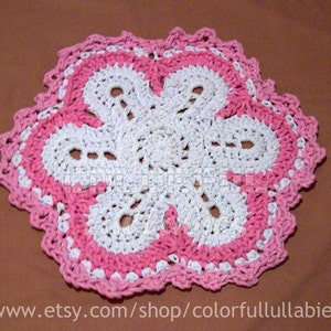 Könnte beinhalten: Eine weiße Häkeldeckchen mit einem rosa Häkelrand. Das Deckchen ist in Form einer Blume mit fünf Blütenblättern.