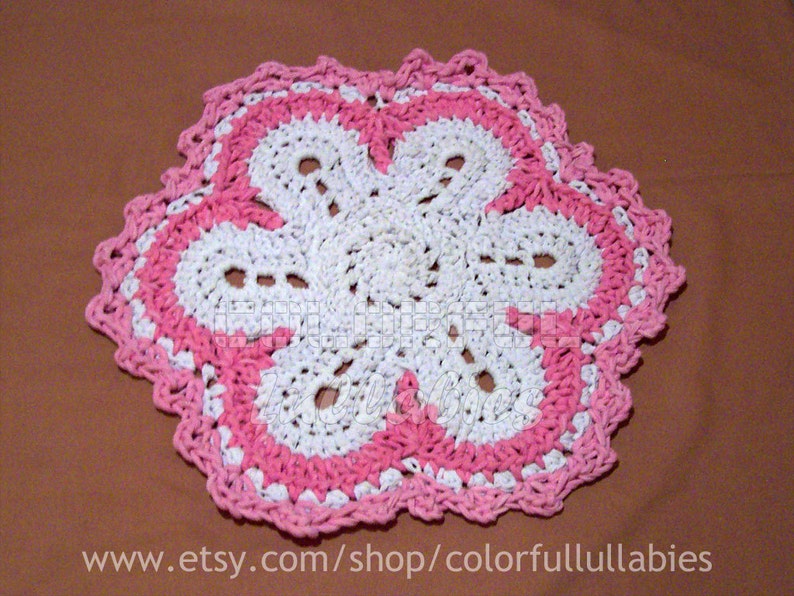 May include: A white crocheted doily with a pink crocheted border. The doily is shaped like a flower with five petals.