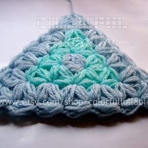 May include: A crocheted triangle with a light blue and teal color gradient. The center of the triangle is teal and the edges are light blue.