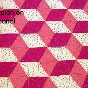 Puede incluir: Una manta de ganchillo con un patrón geométrico 3D en tonos de rosa y blanco.