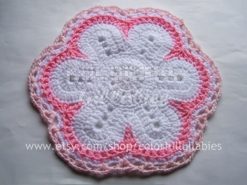 May include: A white crocheted flower with a pink border. The flower has a five-petal design and is made with a delicate stitch.