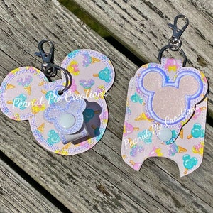 May include: Two pink and white Mickey Mouse shaped keychains with ice cream cone and sprinkle designs. The keychains have a clear plastic window and a snap closure. The text "Peanut Pie Creations" is visible on both keychains.