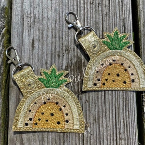 May include: Two gold glitter pineapple keychain charms with green pineapple tops and black polka dots. The charms are attached to silver key rings.