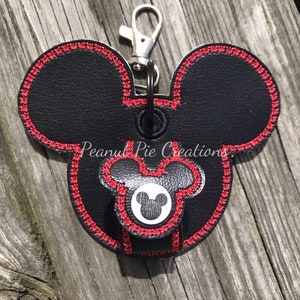 May include: Black faux leather Mickey Mouse keychain with red stitching. The keychain has a metal ring and a silver spring clasp.