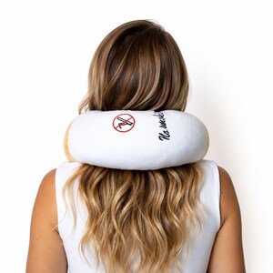 May include: A white travel pillow shaped like a cigarette, with a brown filter and the words "No smoking" in cursive. The pillow has a red "no smoking" symbol embroidered on it.