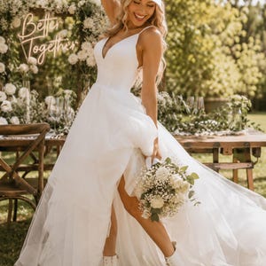 A woman in a white wedding dress with a "BRIDE" hat stands in a garden, holding a bouquet of white flowers.