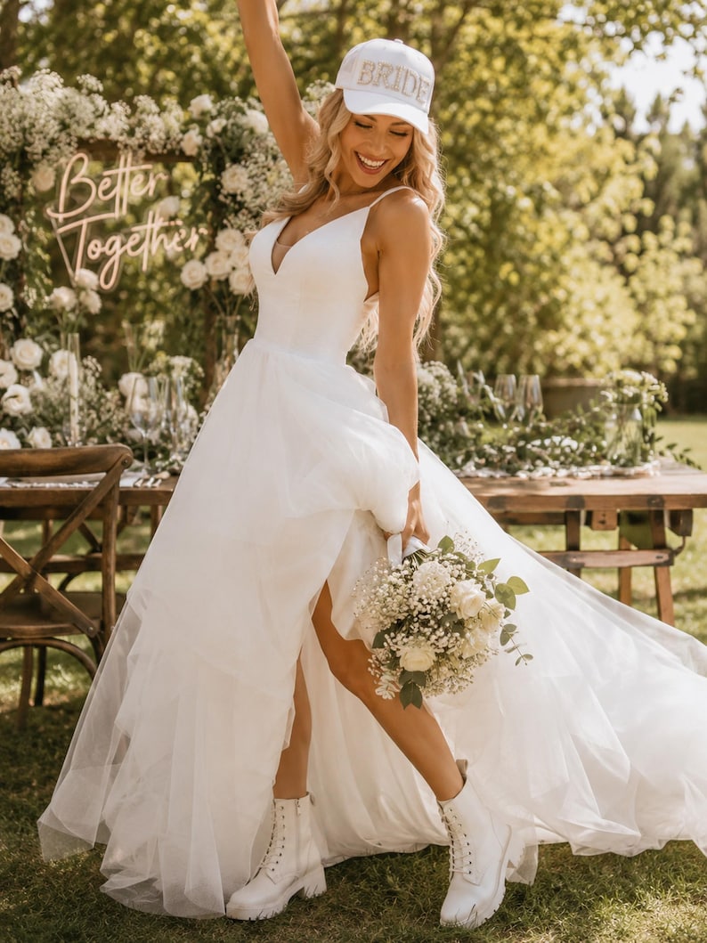 A woman in a white wedding dress with a "BRIDE" hat stands in a garden, holding a bouquet of white flowers.