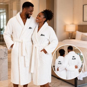 May include: Two white waffle-textured bathrobes featuring black embroidered text. One robe displays 'Mr.' on the front and 'Mr. Smith' on the back, while the other displays 'Mrs.' on the front and 'Mrs. Smith' on the back. Both robes have long sleeves.