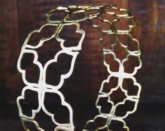May include: A gold-toned metal bracelet with a delicate, intricate design of repeating four-leaf clover shapes.