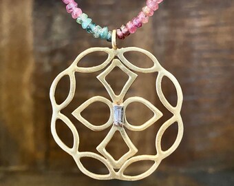 May include: A gold-colored pendant necklace with a geometric design and a small, rectangular gemstone. The necklace features a beaded strand of pink, green, and blue gemstones. The pendant is suspended from the gemstone strand.