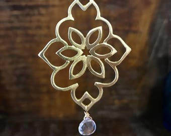 May include: Gold necklace with a large, intricate, geometric pendant featuring a flower design. A clear crystal dangles from the bottom of the pendant.