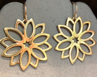 May include: A pair of gold-toned earrings with a delicate, floral design. Each earring features a circular shape with multiple, overlapping petals.