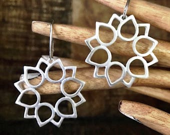May include: A pair of silver earrings with a delicate, circular design featuring eight openwork petals. The earrings have a simple hook closure.