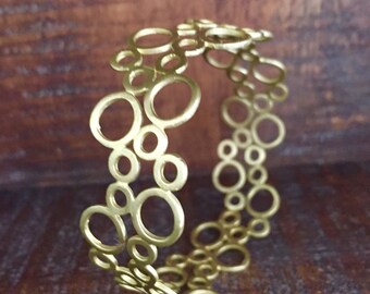 May include: A gold-toned bracelet with a circle pattern. The bracelet is made of metal and has a delicate, airy design.