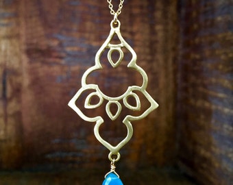 May include: A gold pendant necklace with a delicate, intricate design and a teardrop-shaped blue gemstone.