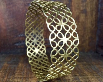 May include: A gold-toned metal bracelet with a delicate, intricate design of overlapping circles and flower shapes.