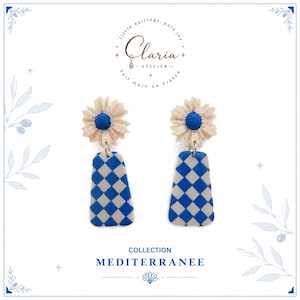 Peut inclure: Une paire de boucles d'oreilles composée d'un clou en forme de marguerite beige avec un centre bleu texturé, attaché à une breloque trapézoïdale pendante à motif damier bleu et beige. Le texte Claria Atelier et Collection Mediterranee est visible.