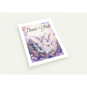 Peut inclure: Une carte de vœux blanche avec l'inscription "Thank You" en écriture élégante. La carte présente une illustration à l'aquarelle d'une licorne ailée planant au-dessus d'un château, d'une cascade et de fleurs colorées.
