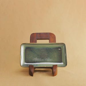 May include: A rectangular ceramic tray with a glossy finish, featuring a gradient of sage green and dark forest green tones. The center of the tray displays a series of horizontal, recessed lines that create a textured, striped pattern across the surface.