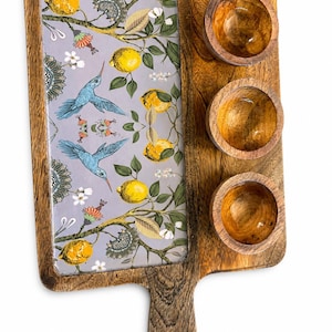 May include: Wooden serving tray with three small bowls and a decorative inset. The inset features a gray background with a lemon and hummingbird design. The tray has a handle and is made of natural wood.