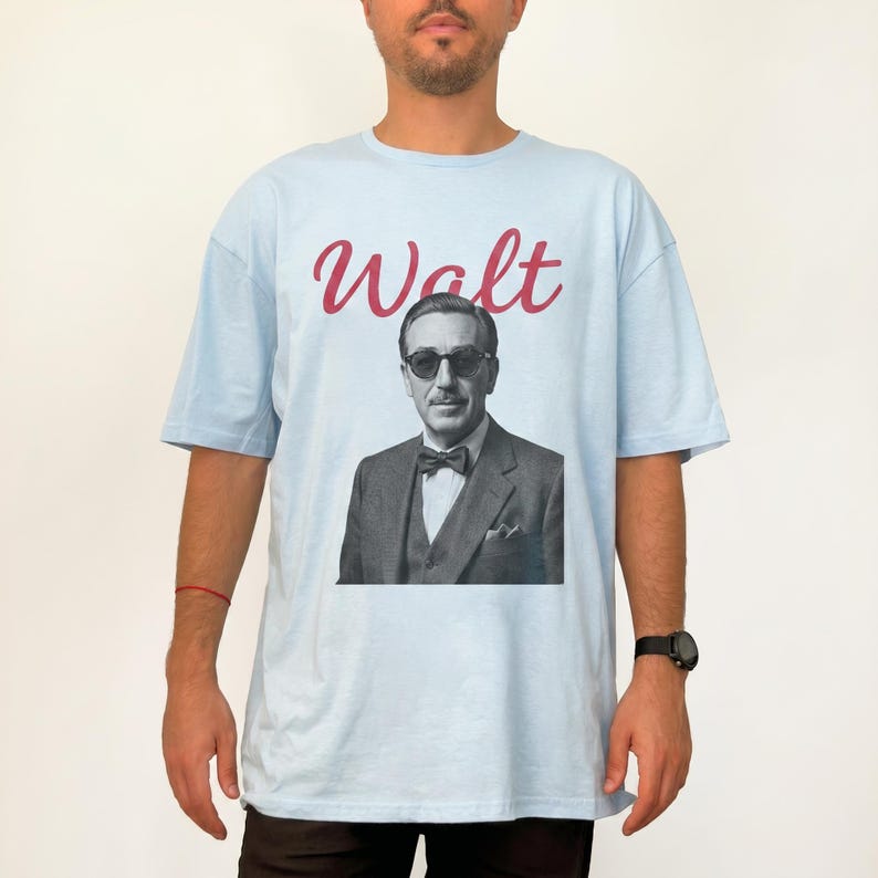 A man wearing a light blue Disney mens shirt. The oversized tee features a classic black and white illustration of Walt Disney with sunglasses and red "Walt" script.
