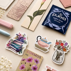 May include: A collection of stationery items including two bookmarks, one with a floral pattern and one with a pink calla lily, a Pukka night time tea bag, a pink heart-shaped leather piece, and several stickers featuring books, flowers, and a teapot.