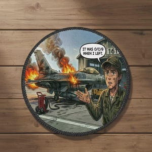 May include: Round patch with a comic illustration of a burning jet plane. A man in a green uniform and cap gestures in front of the plane. Text in a speech bubble reads, "IT WAS O/C/G WHEN I LEFT."