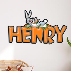 May include: A wall decoration featuring the name "HENRY" in orange block letters with a black outline. The cartoon character Bugs Bunny is lounging on top of the letters, holding a carrot. The background is white.