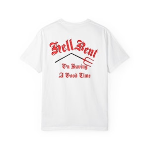 Könnte beinhalten: Weißes T-Shirt mit dem roten Text "Hell Bent On Having A Good Time" in gotischer Schrift. Eine schwarze Linie und ein rotes Mistgabel-Design befinden sich über dem Text. Das Shirt ist ein Freizeitartikel.