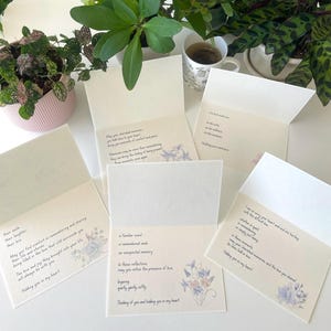 May include: A collection of five open sympathy greeting cards featuring cream-coloured paper with printed black text and delicate watercolour floral illustrations in shades of blue and purple. Each card contains unique messages of comfort and support.