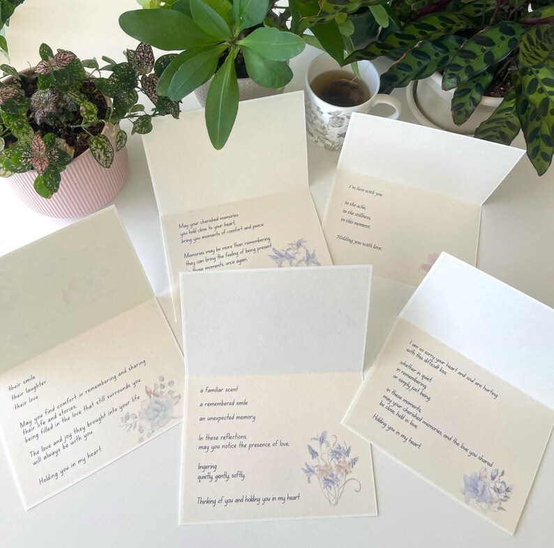 May include: A collection of five open sympathy greeting cards featuring cream-coloured paper with printed black text and delicate watercolour floral illustrations in shades of blue and purple. Each card contains unique messages of comfort and support.