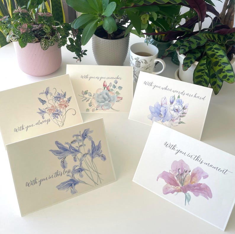 May include: Five white greeting cards featuring watercolour floral illustrations and cursive text. The cards display phrases including With you always, With you as you remember, With you when words are hard, With you in this loss, and With you in this moment.