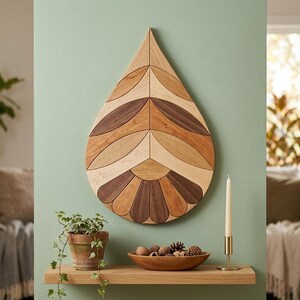 May include: A teardrop-shaped wooden wall art piece composed of various light, medium, and dark wood segments arranged in a symmetrical, leaf-like pattern. The wood grain is visible throughout the geometric design, which features pointed top and rounded bottom edges.