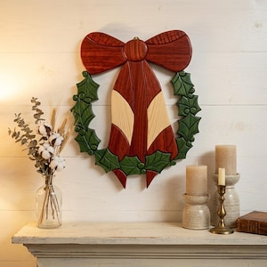 Puede incluir: Corona navideña de madera con un gran lazo rojo y un diseño en forma de campana. La corona presenta hojas verdes de acebo y está montada en una pared blanca. El diseño incorpora tonos de madera natural y es una decoración festiva.