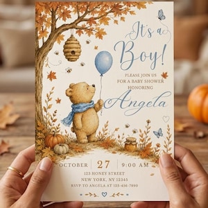 Pode incluir: Um convite de chá de bebê com um urso marrom claro usando um cachecol azul, segurando um balão azul sob uma árvore de outono com uma colmeia. O texto diz: It's a Boy! Please join us for a baby shower honoring Angela, October 27, 9:00 AM.