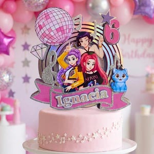 Könnte beinhalten: Ein rosafarbener Tortenaufleger mit drei illustrierten Figuren, einer Discokugel, Musiknoten, einem violetten Stern und der Zahl 6. Ein rosa Banner am unteren Rand zeigt den Namen Ignacia in weißen Buchstaben auf einer hellrosa Torte.