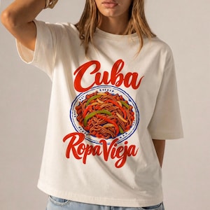 May include: An off-white short-sleeve t-shirt featuring a graphic print of a plate of Ropa Vieja. The text Cuba is printed in red above the plate, and Ropa Vieja is printed in red below the plate. The graphic includes red and green peppers.