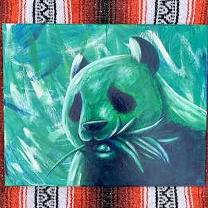 May include: A green and blue painting of a panda bear eating bamboo. The panda's face is detailed with black eyes and ears, set against a background of abstract brushstrokes. The artwork is on a canvas.